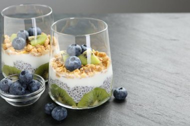 Süper yemek. Chia tohumlu lezzetli tatlı, yoğurt, granola, yaban mersini ve kivi gri masada, yakın plan. Metin için boşluk