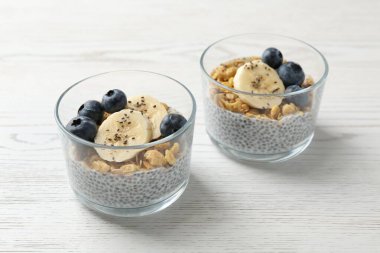 Chia tohumlu lezzetli tatlı, yoğurt, granola, yaban mersini ve muz beyaz ahşap masada, yakın plan. Süper yemek.