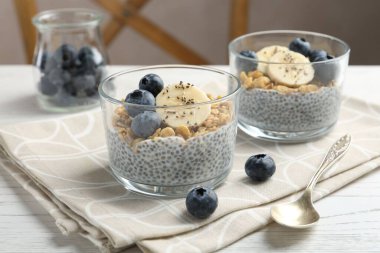 Chia tohumlu lezzetli tatlı, yoğurt, granola, yaban mersini ve muz beyaz ahşap masada, yakın plan. Süper yemek.