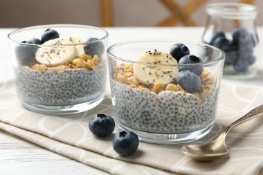 Chia tohumlu lezzetli tatlı, yoğurt, granola, yaban mersini ve muz beyaz ahşap masada, yakın plan. Süper yemek.