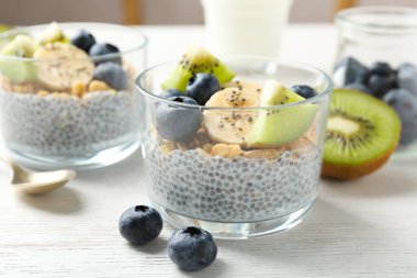 Chia tohumlu lezzetli tatlı, yoğurt, granola, yaban mersini, muz ve kivi beyaz ahşap masada, yakın plan. Süper yemek.