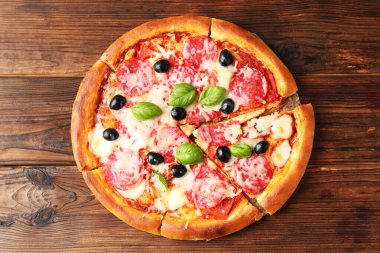 Tahta masada salamlı, peynirli, fesleğenli ve zeytinli lezzetli pizza.