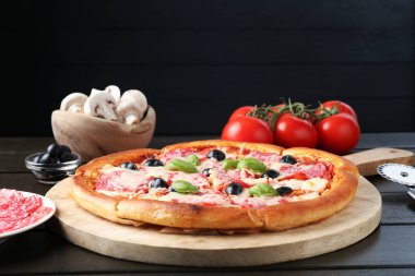 Lezzetli pizza, malzemeler ve siyah ahşap masa, yakın plan.