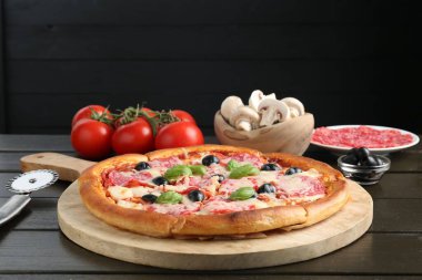 Lezzetli pizza, malzemeler ve siyah ahşap masa, yakın plan.