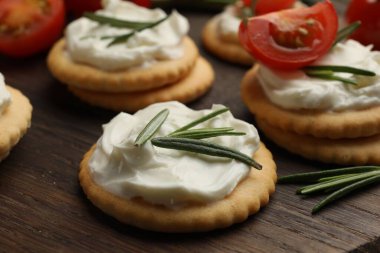 Krem peynirli krakerler, biberiye ve domatesler ahşap masada, yakın plan.