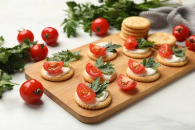 Krem peynirli krakerler, domatesler ve maydanozlar beyaz masada, yakın plan.