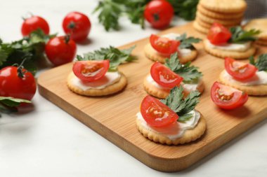 Krem peynirli krakerler, domatesler ve maydanozlar beyaz masada, yakın plan.