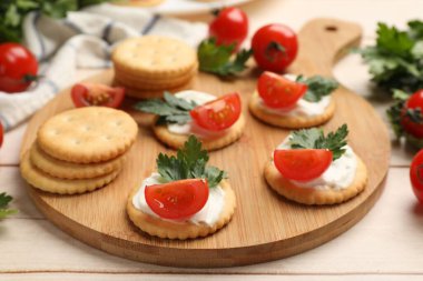 Krem peynirli krakerler, domatesler ve maydanozlar beyaz ahşap masada, yakın plan.