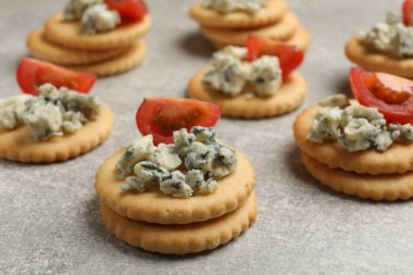 Lezzetli krakerler, mavi peynirli ve domatesli gri desenli masa, yakın plan.