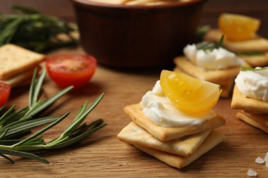 Krem peynirli krakerler, biberiye, ahşap masada tuz ve domatesler, yakın plan.