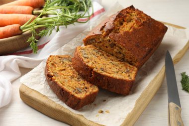 Beyaz ahşap masada fındıklı, sebzeli ve bıçaklı ev yapımı havuçlu kek, yakın plan.