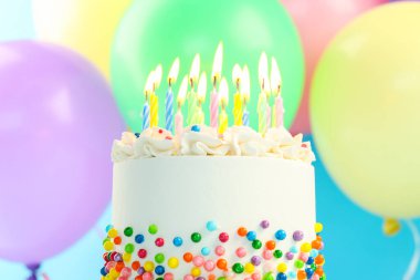 Enfes bento keki serpiştirilmiş, yanan mumlar ve açık mavi arka planda renkli balonlar, yakın plan.