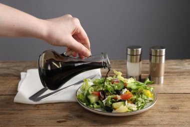 Ahşap masadaki salataya balzamik sirke döken kadın, yakın plan, gri arka plan...