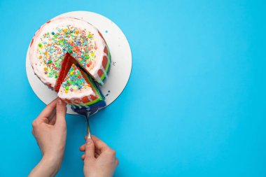 Açık mavi masada spatulayla lezzetli bir gökkuşağı pastası yiyen bir kadın. Metin için boşluk