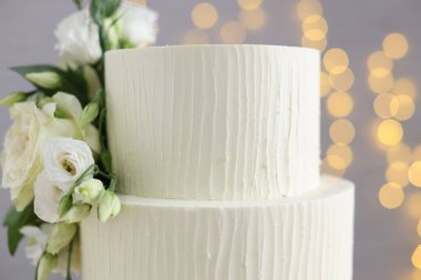 Gri arka planda çiçeklerle süslenmiş enfes düğün pastası. Bulanık ışıklar, yakın plan.