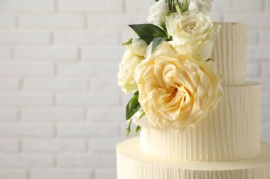 Beyaz tuğla duvarın yanında çiçeklerle süslenmiş nefis düğün pastası, yakın plan. Metin için boşluk