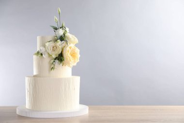Gri arka planda, ahşap masada çiçeklerle süslenmiş lezzetli düğün pastası. Metin için boşluk
