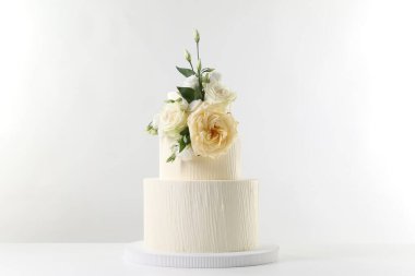 Masada beyaz arka planda çiçeklerle süslenmiş lezzetli düğün pastası.