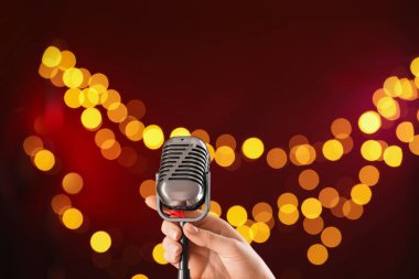 Koyu kırmızı arka planda klasik mikrofonu olan, bulanık ışıkları olan, yakın plan ve mesaj için yeri olan bir kadın. Bokeh etkisi