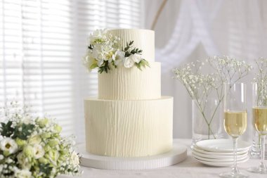 Çiçek desenli nefis düğün pastası, çiçek buketi ve kapalı bir masada bir bardak şampanya.