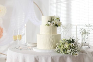 Çiçek desenli nefis düğün pastası, çiçek buketi ve kapalı bir masada bir bardak şampanya.