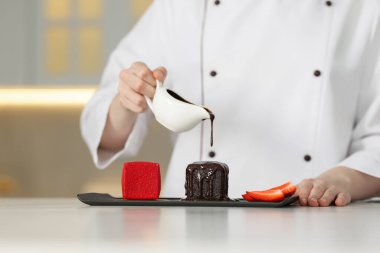 Şekerci, mutfaktaki beyaz mermer masada lezzetli tatlıların üzerine çikolata sosu döküyor.