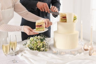 Yeni evliler kapalı bir masada düğün pastası kesiyorlar.