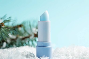 Nemlendirici dudak kremi ve yapay kar üzerindeki köknar ağacı dalları açık mavi arka planda, yakın plan. Kış bakımı