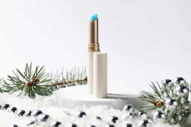 Nemlendirici dudak kremi, Noel dekorasyonu ve beyaz arka planda suni kar üzerindeki köknar ağacı dalları, yakın plan. Kış bakımı