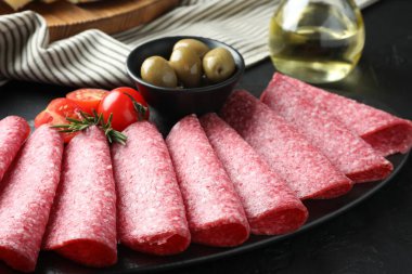 Siyah masada servis edilen zeytinli ve domatesli leziz sosis dilimleri.