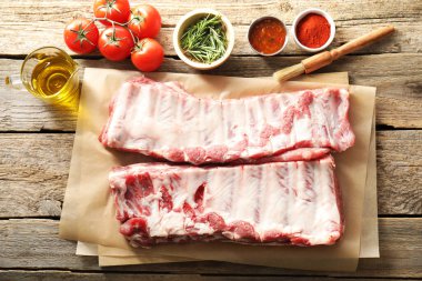 Çiğ domuz kaburgası, baharatlar ve domatesler ahşap masada, düz yatıyordu.