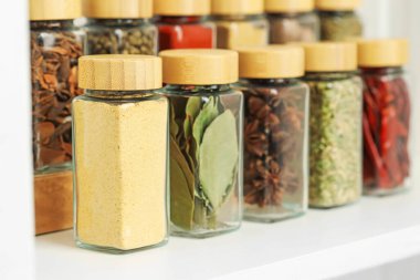 Beyaz masadaki kavanozlardaki farklı aromatik baharatlar, yakın plan.