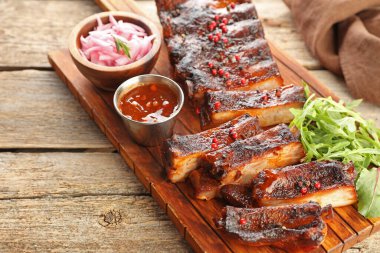 Lezzetli domuz pirzolası, roka, sos ve soğan ahşap masada, yakın plan.