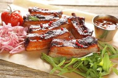 Lezzetli domuz kaburgası, sos, roka ve soğan ahşap masada, yakın plan.