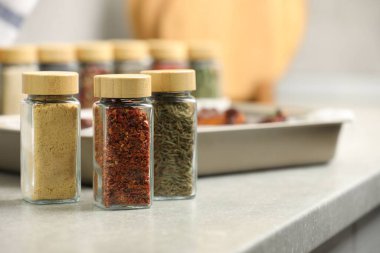 Kavanozlardaki farklı aromatik baharatlar ve açık gri masa üzerindeki tabak, metin için yer