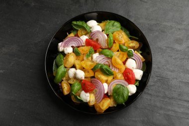 Sarı domatesli lezzetli salata, fesleğen, soğan ve siyah masada mozzarella peyniri.