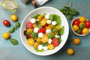 Sarı domatesli lezzetli salata, fesleğen ve mozzarella peyniri açık mavi ahşap masa üzerinde.