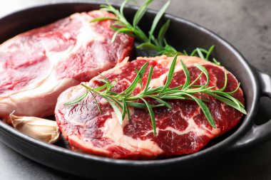 Gri masadaki pişirme kabında çiğ et ve baharat parçaları, yakın plan.