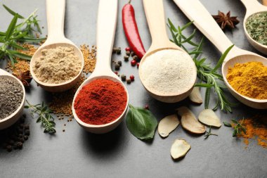 Gri masadaki kaşıklardaki farklı baharatlar, yakın plan.