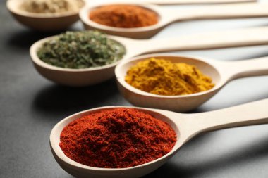 Gri masadaki kaşıklardaki farklı baharatlar, yakın plan.