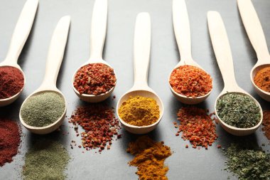 Gri masadaki kaşıklardaki farklı baharatlar, yakın plan.