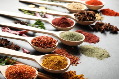 Gri masadaki kaşıklardaki farklı baharatlar, yakın plan.