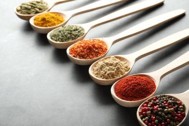 Gri masadaki kaşıklardaki farklı baharatlar, yakın plan.