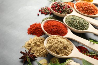 Gri masadaki kaşıklardaki farklı baharatlar, yakın plan.