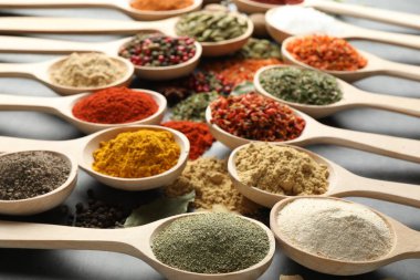 Gri masadaki kaşıklardaki farklı baharatlar, yakın plan.