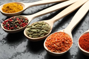 Siyah masadaki kaşıklardaki farklı baharatlar, yakın plan.