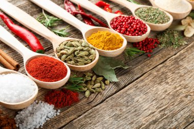 Tahta masadaki kaşıklardaki farklı aromatik baharatlar, yakın plan.