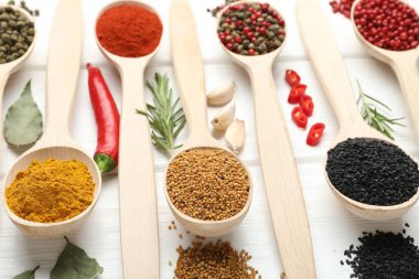 Beyaz ahşap masadaki kaşıklarda farklı aromatik baharatlar, yakın plan.