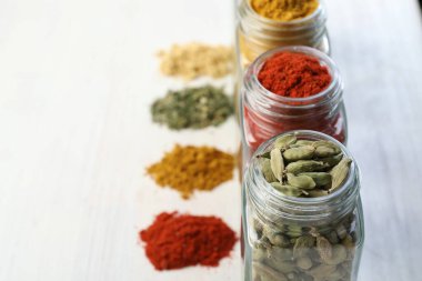 Beyaz masadaki kavanozlarda farklı aromatik baharatlar, yakın plan. Metin için boşluk