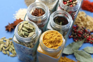 Mavi arka planda kavanozlardaki farklı aromatik baharatlar, yakın plan.